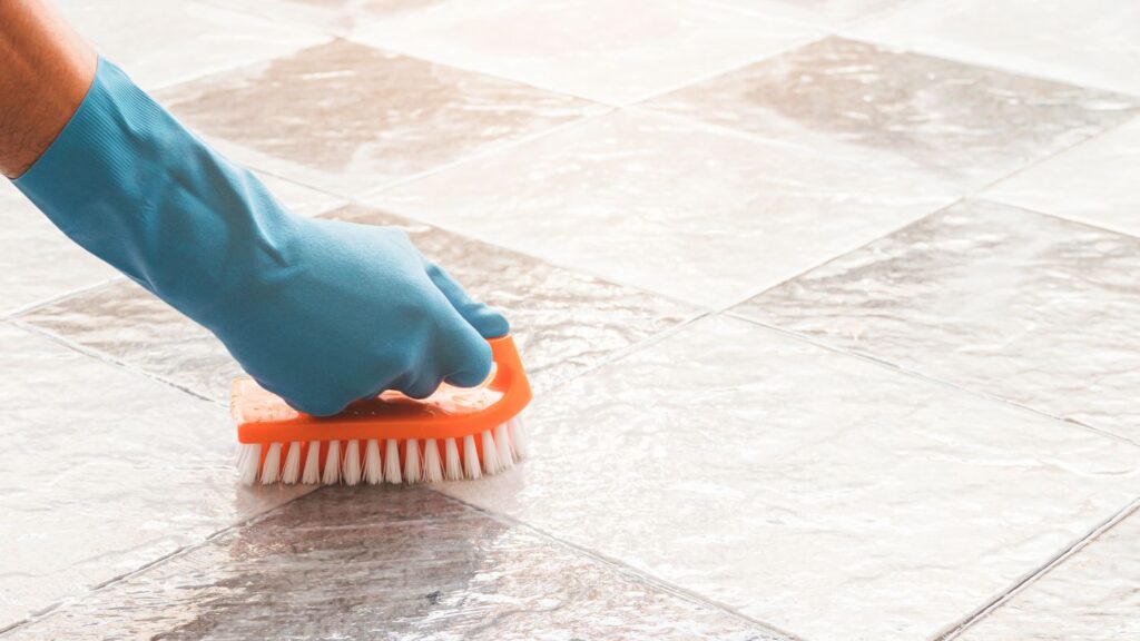 A hand in a blue glove scrubs tile floor.