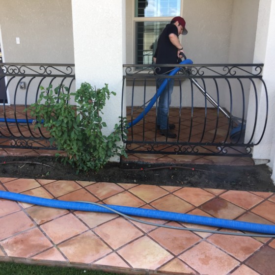 A man cleaning tile patio with a vacuum.