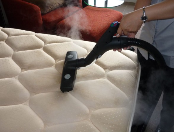 Steam cleaning a mattress with a machine.