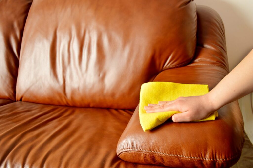 Hand cleaning brown leather couch.