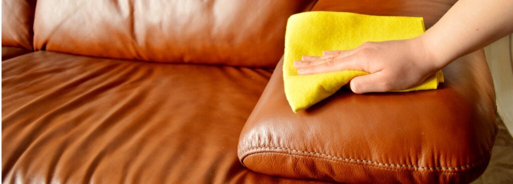 Hand wiping brown leather couch with yellow cloth.