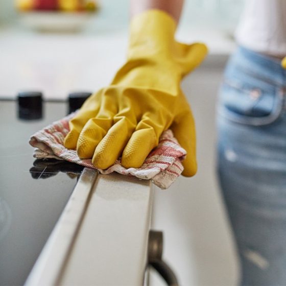 Person cleaning a stovetop with gloves.